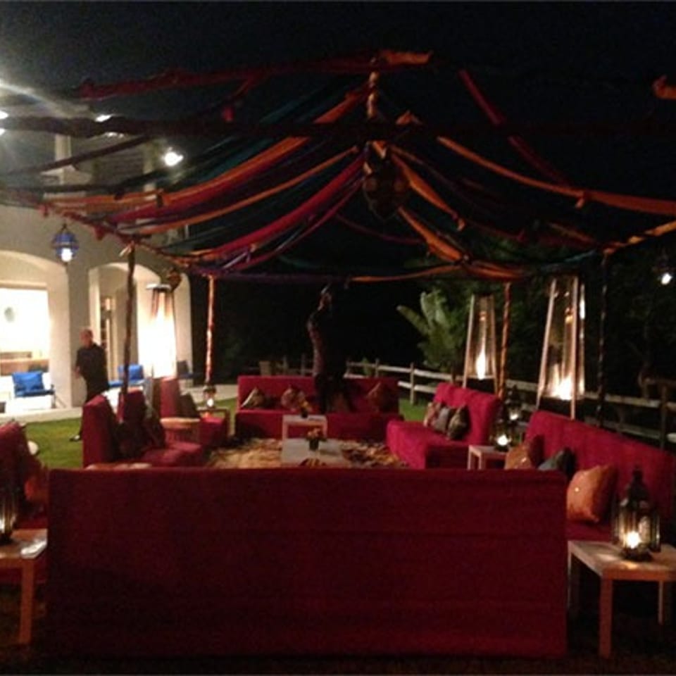Outdoor restaurant lounge at night with red sofas, lanterns, and colorful fabric draped across the canopy.