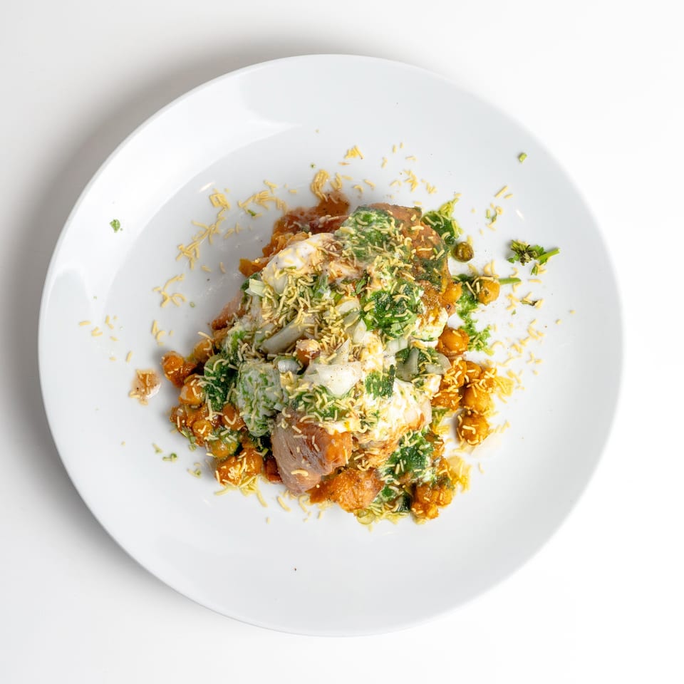 A colorful Indian chaat dish with chickpeas, sauces, and crispy noodles on a white plate.