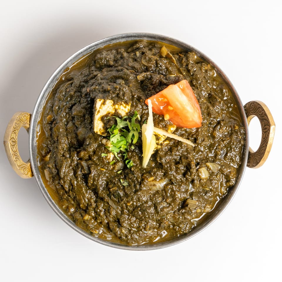 Palak paneer, a spinach and cheese curry, garnished with tomato, ginger, and cilantro.