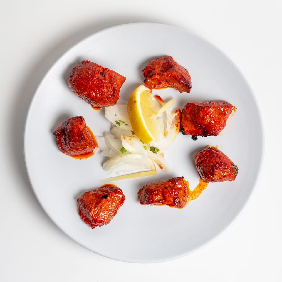 Red marinated chicken tikka pieces with sliced onions and a lemon wedge on a white plate.