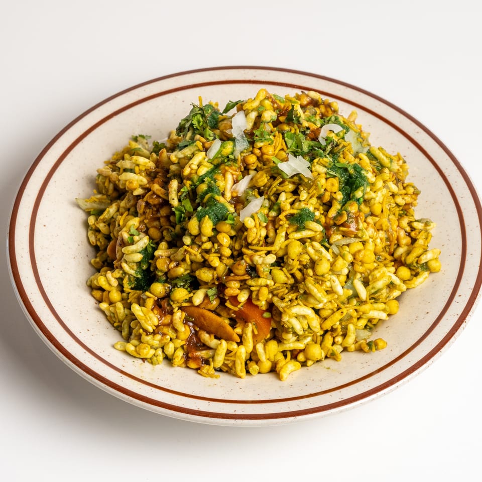 A close-up of a colorful Indian snack mix with puffed rice, spices, and herbs on a plate.