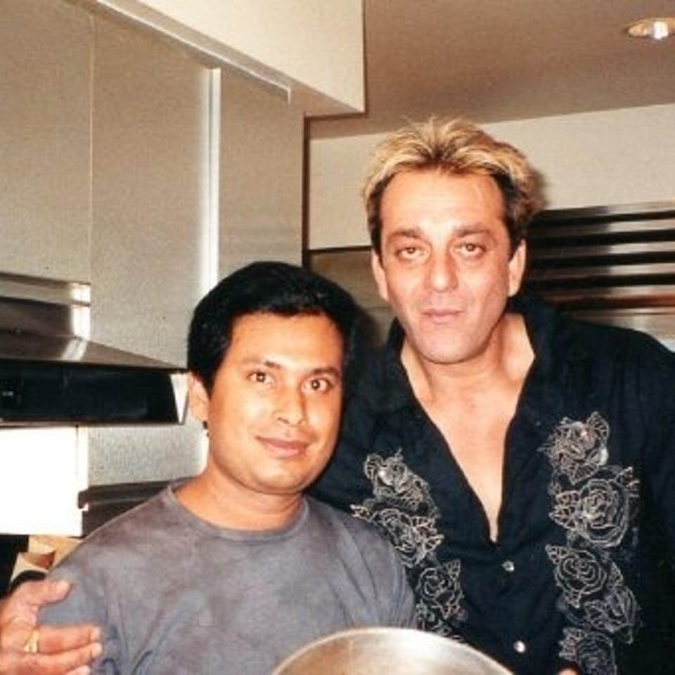Two men pose in a commercial restaurant kitchen, with one holding a large metal bowl.